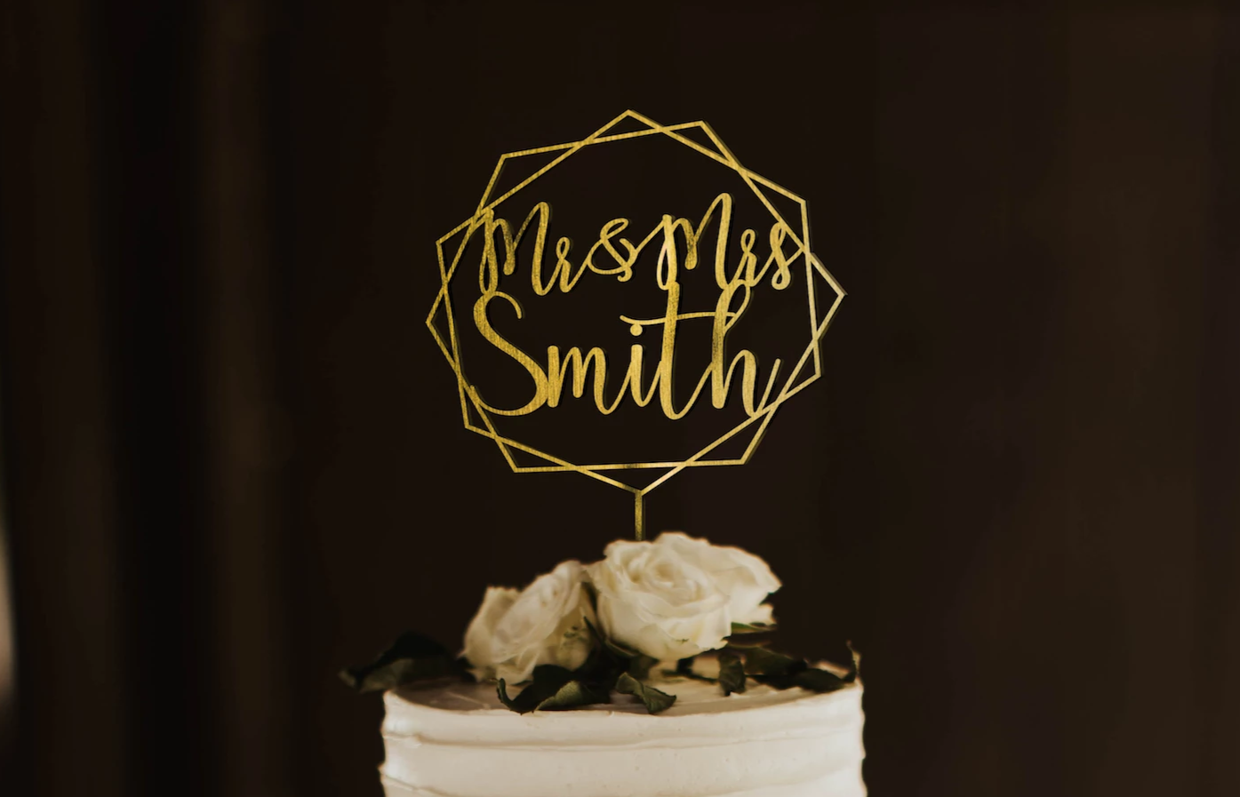 calligraphy personalized golden hexagon wreath style cake topper made of wood on top of the white simple wedding cake. 