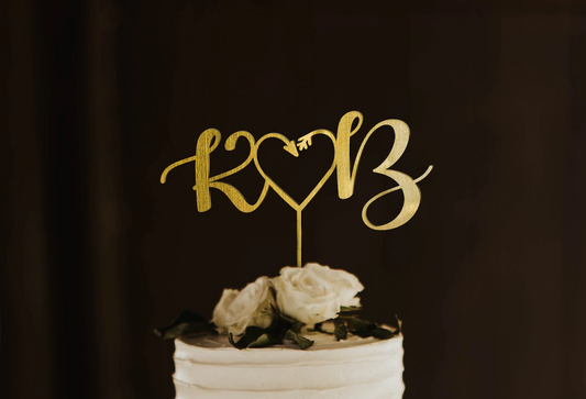 calligraphy personalized golden monogram style cake topper made of wood on top of the white simple wedding cake. 