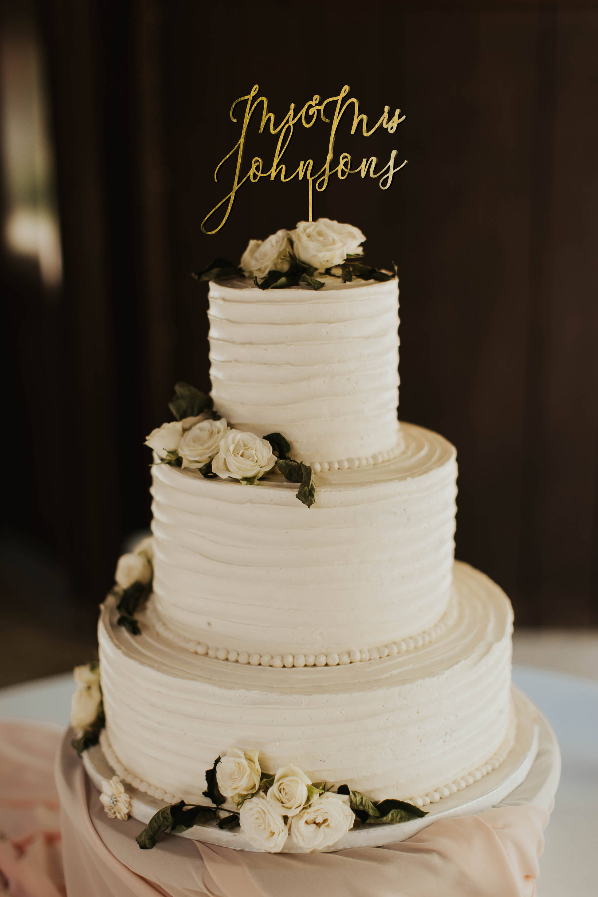 thin calligraphy personalized golden cake topper made of wood on top of the white simple wedding cake. 